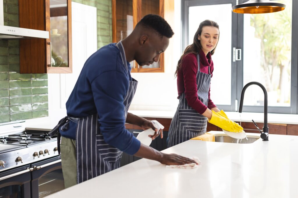 Happy diverse couple cleaning countertop and doing dishes in kitchen at home
